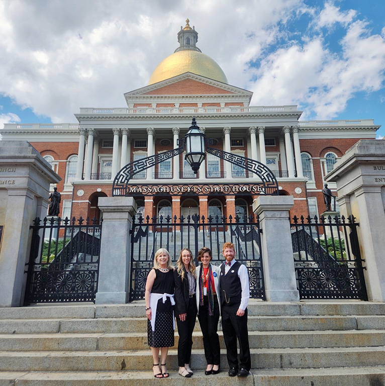 Four GLFHC staff outside in front of the Massachusetts State House on the steps with the gold dome in the background.