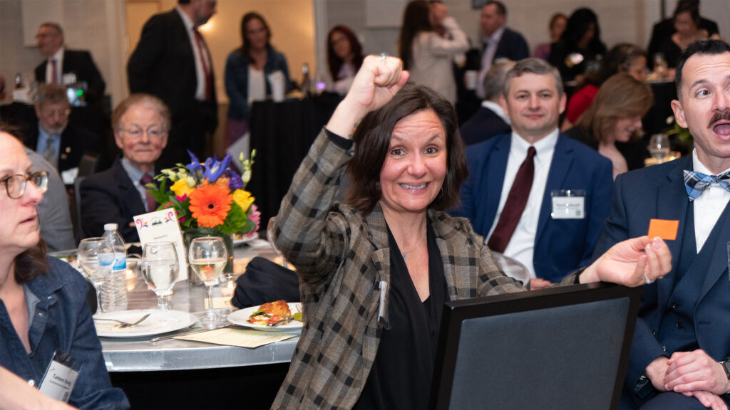 A woman with her fist in the air has won a raffle prize at GLFHC's Spring Benefit 2026.